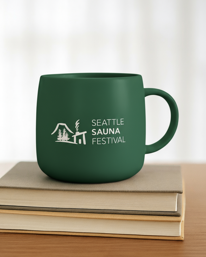 Green mug with 'Seattle Sauna Festival' logo on a stack of books